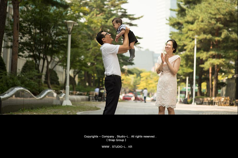 아빠가 돌잔치 당일 아기를 도심 공원에서 번쩍 들어올리는 장면