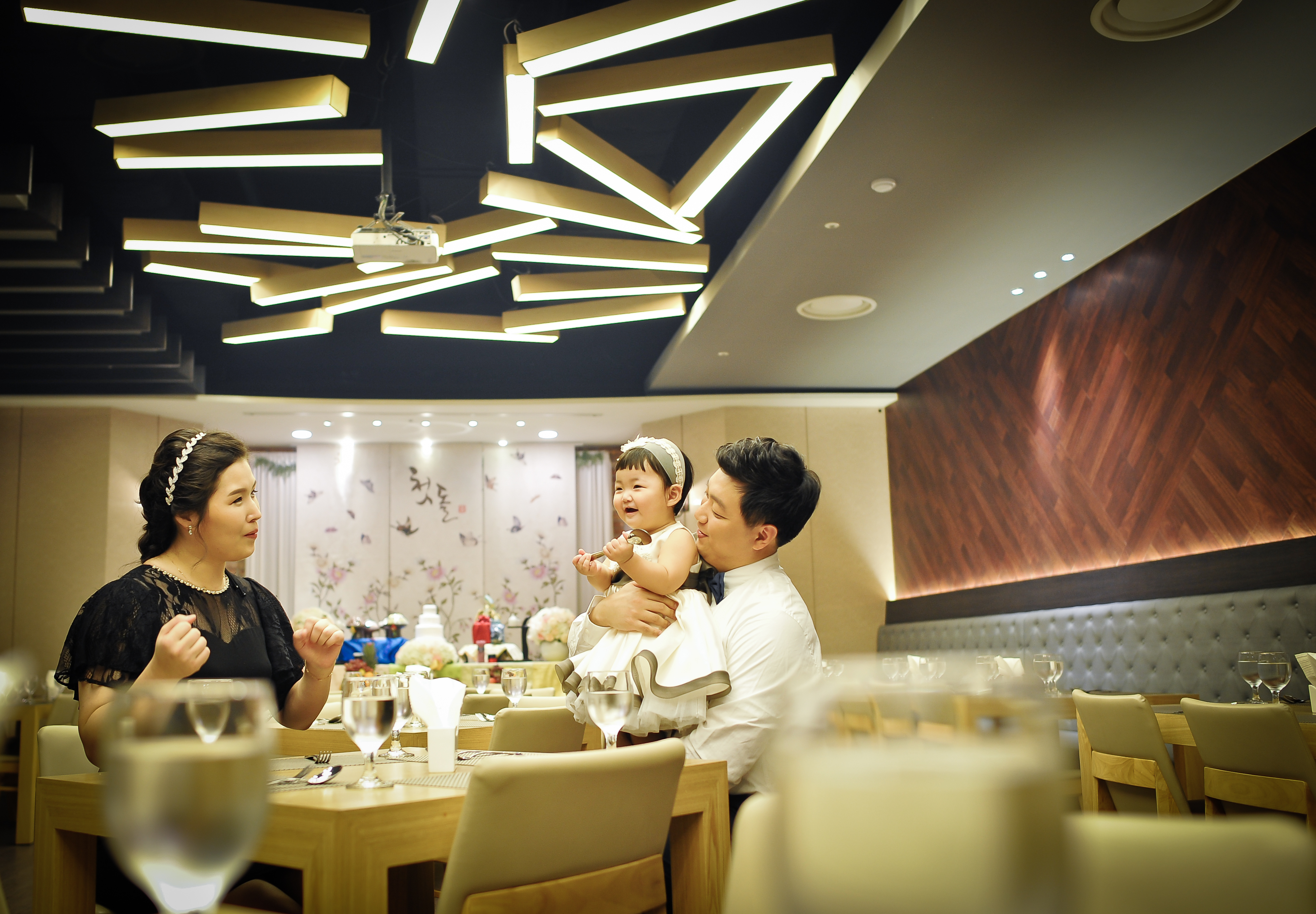 돌잔치홀 천장 조명 아래 부모와 함께 앉은 라함이