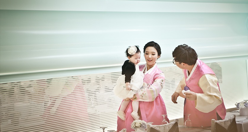 분홍 한복의 엄마와 아빠, 검정 한복의 아기, 밝은 돌잔치홀