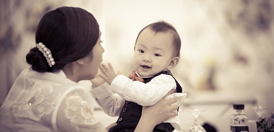 엄마 손 위에 앉은 우준이 클로즈업 — 수트 차림, 웃는 표정