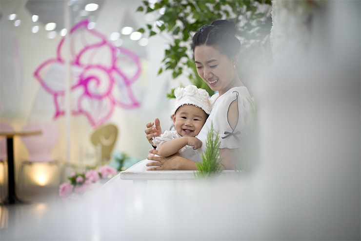 플로럴 세트장에서 엄마 품 안 아이 — 흰 드레스와 꽃 헤드밴드, 활짝 웃는 표정