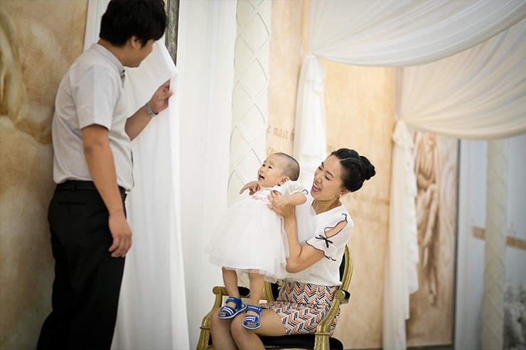 흰 드레이프 세트에서 엄마 무릎에 앉은 아이 — 아빠 옆에 서 있고 아이 옹알이 표정