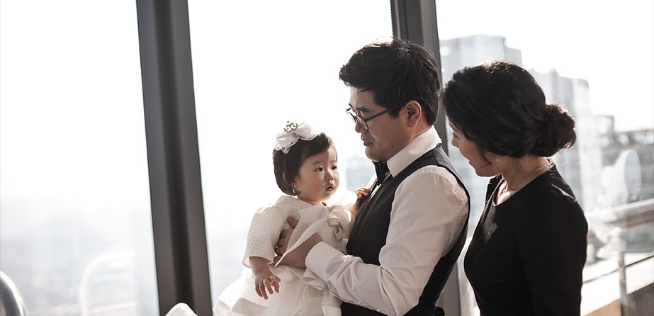 창가 역광 — 아빠 품의 승아, 엄마가 곁에 선 3인 컷