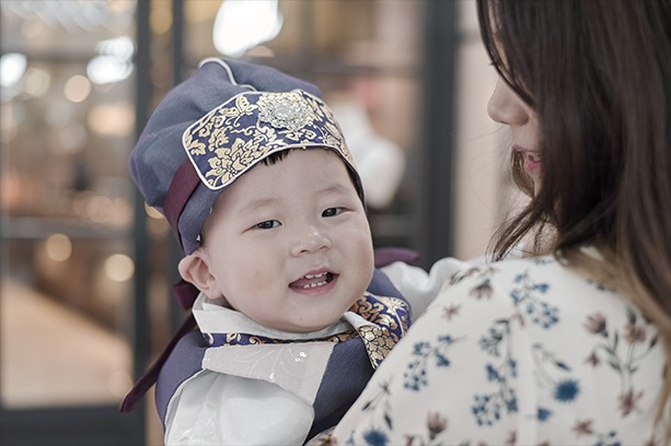 돌잔치홀 입구에서 엄마 품에 안긴 예운이 — 복건 한복 차림 클로즈업