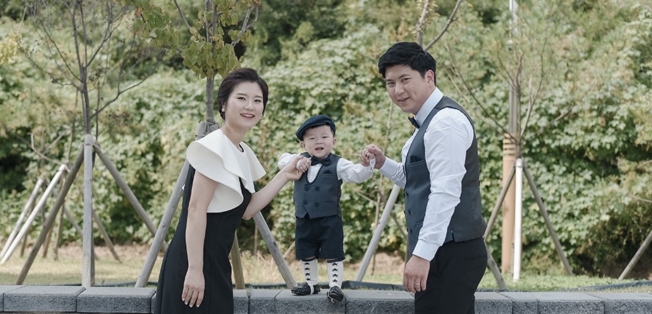 야외 정원에서 수트 차림 예운이 — 부모님과 양손 잡고 선 전체 컷