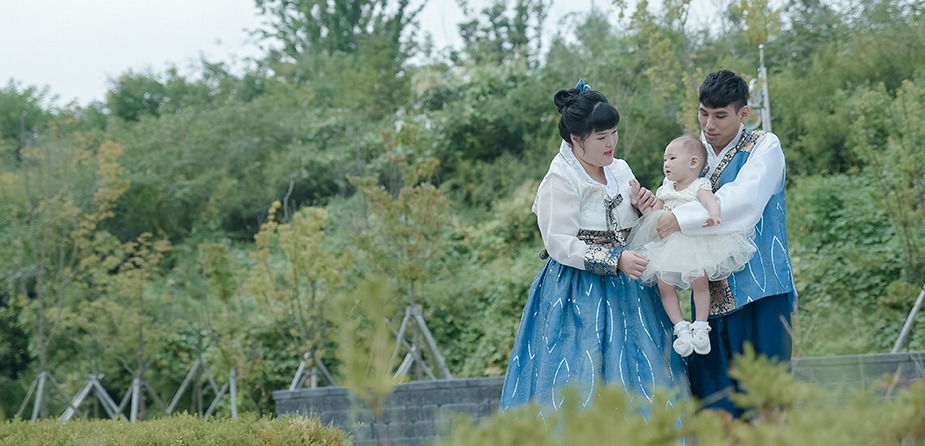 부모 한복 차림으로 예빈이를 함께 안고 있는 3인 전신 컷 — 녹지 배경
