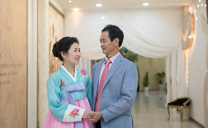 돌잔치홀 복도 — 부부가 서로 마주보며 손을 잡는 장면