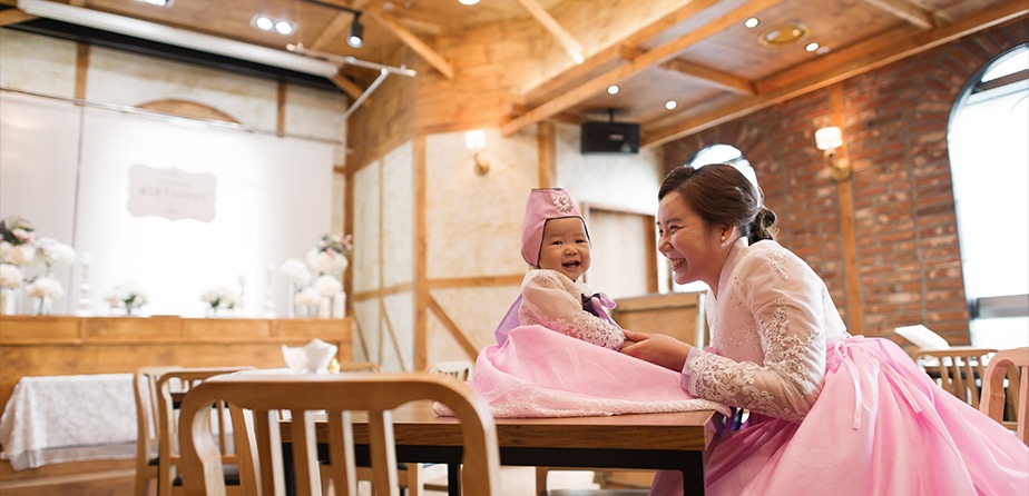 실내 돌잔치홀 한복 컷 — 엄마와 하윤이 테이블 앞, 함께 웃는 순간, 장식 배경