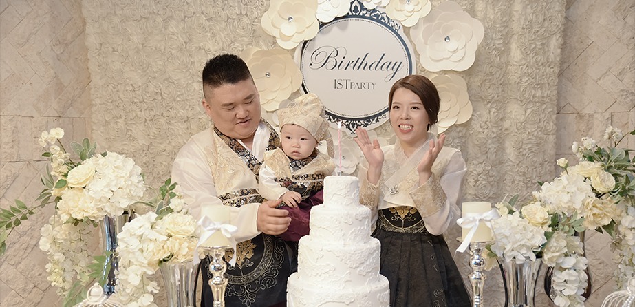 돌잔치홀 케이크 테이블 앞 가족 3인 — Birthday 백드롭, 꽃 장식